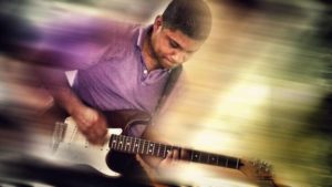 Angel Sanchez Guitar playing his stratocaster guitar with a motion blurred background in estrena sitio web